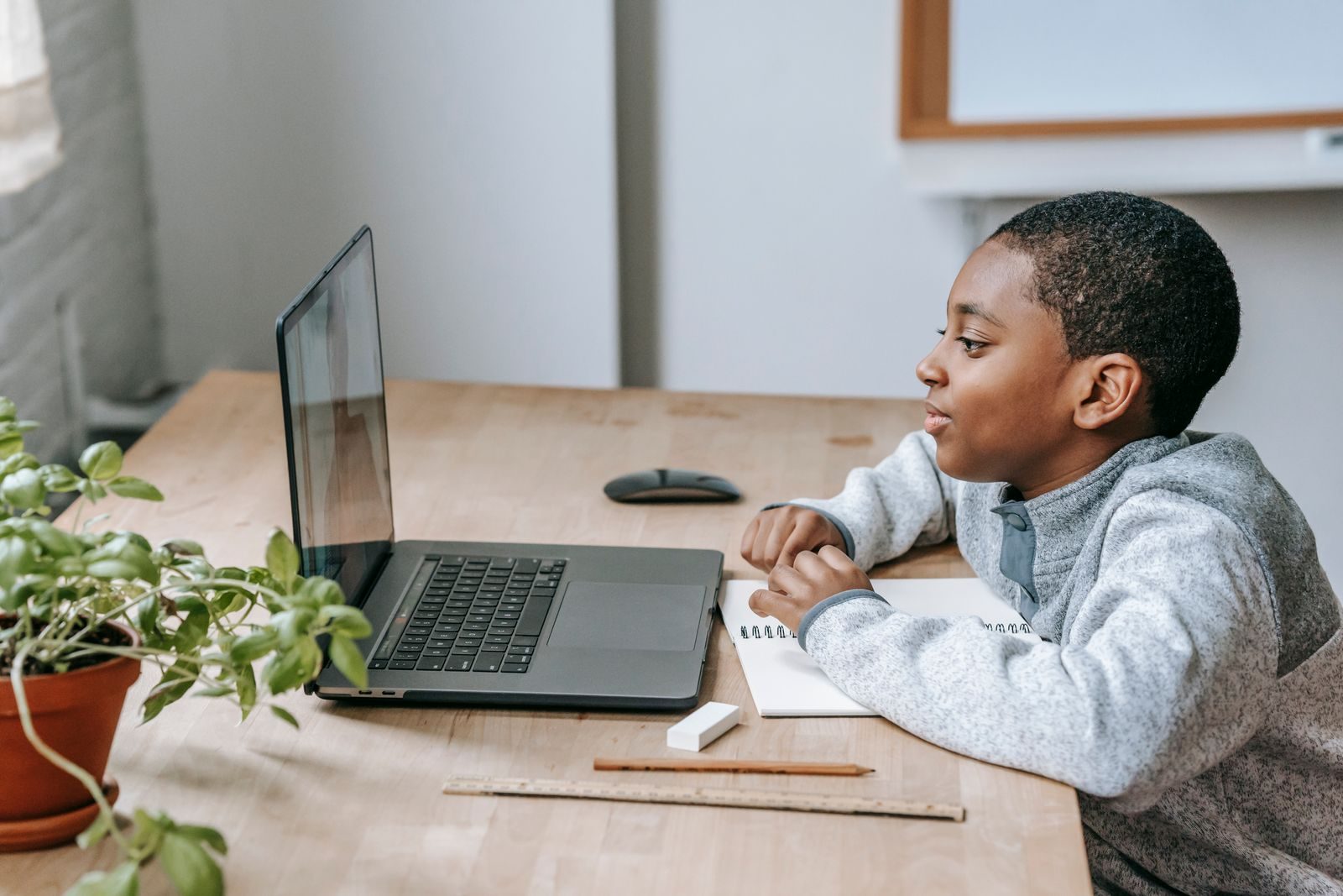 A learner studying at a home desk with a laptop and notebook